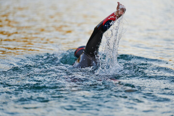 Triathlon athlete swimming on lake in sunrise wearing wetsuit