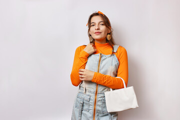 A beautiful cheerful girl poses in front of the camera in a denim suit and an orange t-shirt with a...
