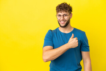 Young handsome caucasian man isolated on yellow background giving a thumbs up gesture