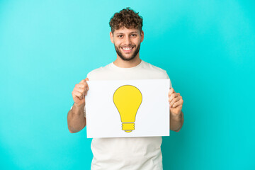 Young handsome caucasian man isolated on blue background holding a placard with bulb icon with...