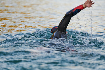 Triathlon athlete swimming on lake in sunrise wearing wetsuit