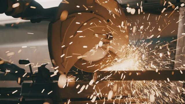 Man works circular saw. Industrial professional worker grinding metal. Craftsman sawing metal with disk grinder in workshop. Sparks fly from hot metal. Slow motion. 4K