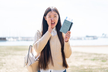 Young Chinese woman holding a passport at outdoors shouting with mouth wide open