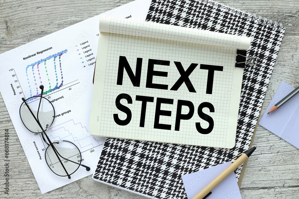 Poster next steps notepad on a wooden table. text on page on financial chart