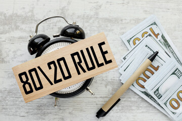 80 20 Rule money bills and pen. top view of wooden block on table clock
