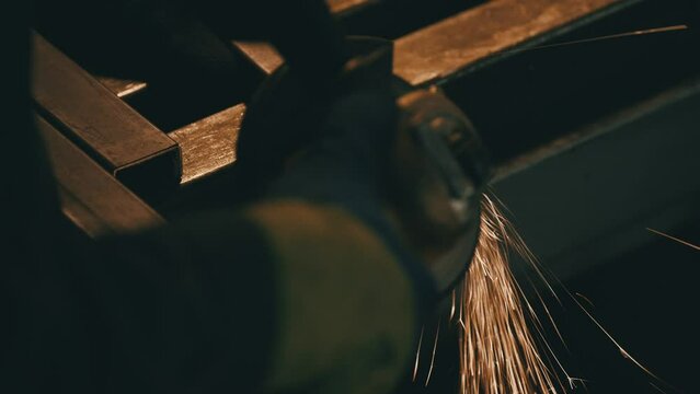 Worker grinding iron. Heavy industry factory interior with worker using an angle grinder with lots of sharp sparks. Electric wheel grinding on steel pipe in factory. Slow motion. 4K video
