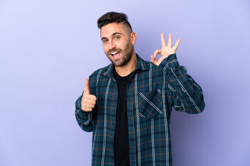 Caucasian man isolated on purple background showing ok sign and thumb up gesture
