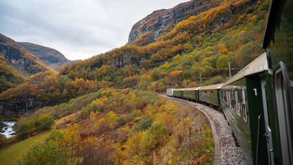 Side view of a train running on a track on a hairpin bend in the fjord mountains of Norway in autumn.