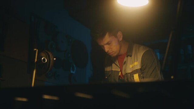 A male engineer works with drawings lying on a steel table in a dark workshop with full equipment, using a pencil. Working indoors on new product prototype in metal manufactory. 4K