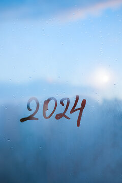numbers 2024 of new year paint with finger on foggy glass on blue sunset window