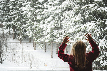Ein kleines Mädchen steht am Fenster uns beobachtet den Schneefall
