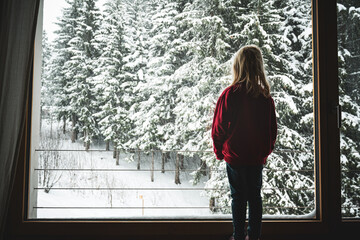 Ein kleines Mädchen steht am Fenster uns beobachtet den Schneefall
