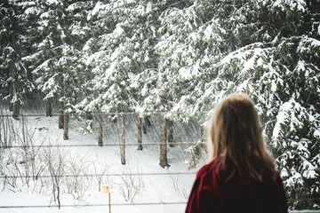 Ein kleines Mädchen steht am Fenster uns beobachtet den Schneefall
