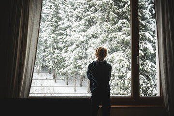 Ein Junge steht am Fenster und beobachtet den Schneefall - obrazy, fototapety, plakaty