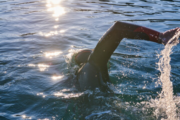 Triathlon athlete swimming on lake in sunrise wearing wetsuit