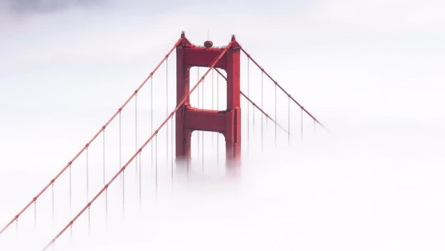 Cinematic bridge covered by dense thick fog with San Francisco downtown on background. Aerial red tall tower of Golden Gate Bridge in scenic white cloud USA.Helicopter overhead red bridge on sunny day