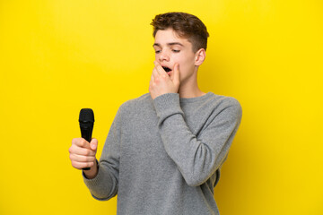 Singer Teenager man picking up a microphone isolated on yellow background with surprise and shocked...