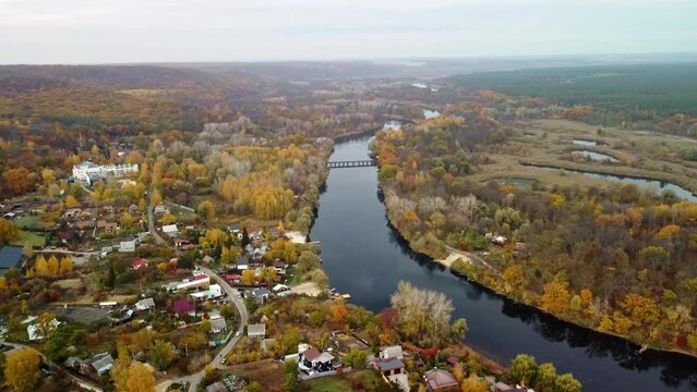 Aerial forward view on river with autumn trees and recreation area in Korobovy Hutora (Koropove village). Car bridge across Siverskyi Donets River in Ukraine