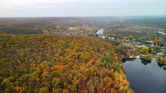 Aerial speedup forward view on river with autumn vibrant trees and recreation area in Korobovy Hutora (Koropove village). Siverskyi Donets River in Ukraine