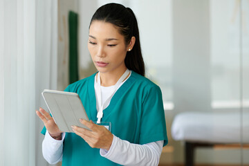 Portrait of young nurse reading medical history of patient on tablet computer