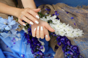Pearl manicure on short square nails on a blue background with a bouquet of irises.