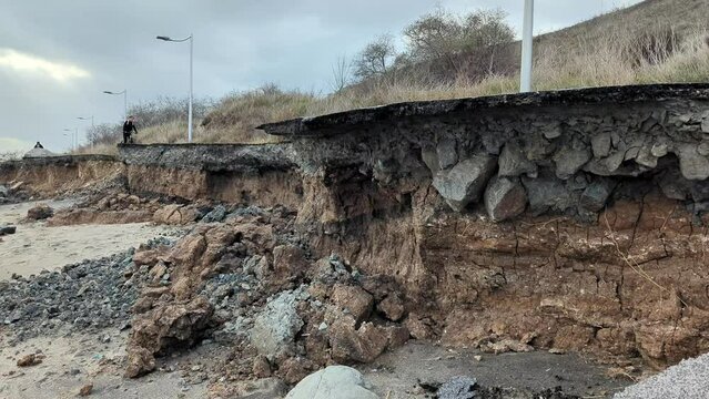 destroyed pedestrian asphalt road, erosion of soil without reinforcement along the coastline