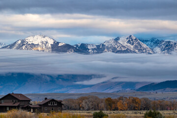 Log cabins with a forest view and low level cloud, snow covered mountains on the outskirts of Yellowstone national park on a cold autumn's day