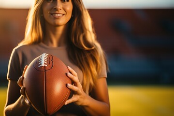 Smiling woman holding an American football ball. A charming young girl with long brown hair wearing...