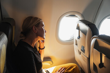 Passenger woman is flying in plane. Girl sitting in airplane looking out window going on trip...