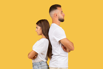 Sad angry millennial european wife and husband in white t-shirts back to back, ignoring after quarrel