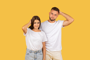 Pensive sad confused young european man and lady in white t-shirts scratches head