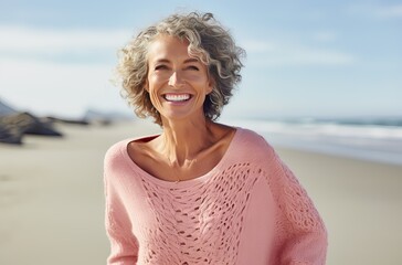 portrait of a well-groomed mature woman with white curly hair and a pink sweater at the beach