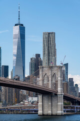 Low angle view from waterfront Brooklyn Bridge Park to the Brooklyn Bridge in Lower Manhattan, New York City, USA with skyscrapers of Lower Manhattan, Two Bridges and Financial district in background