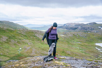 Obraz premium Mature woman is going to dress up with warmer clothes, hiking at high altitude cold high altitude Norwegian Mountains range terrain. Hiking high in Norwegian mountains. Norway, Krutvatnet. Front view