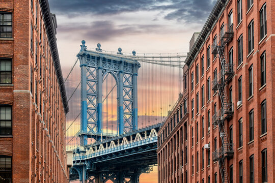Fototapeta Iconic view of Manhattan Bridge, New York City, USA seen from Washington Street in Dumbo (Down Under the Manhattan Bridge Overpass), Brooklyn with clouds coloring orange during sunset