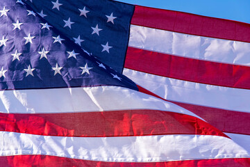 Fototapeta premium Close up of the fabric of an American flag that flutters in the wind with red and white stripes and stars in blue sky