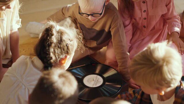 Close-up shot of preschool children sitting after the record player looking at it and listening to music. The Children learn music