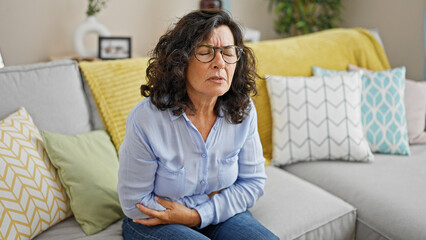 Middle age hispanic woman suffering for stomach ache sitting on sofa at home