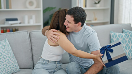 Fototapeta premium Beautiful couple sitting on sofa surprise with birthday gift at home