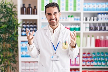 Handsome hispanic man working at pharmacy drugstore celebrating mad and crazy for success with arms...