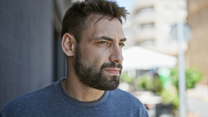 Fototapeta premium Cool and handsome young hispanic man, with a relaxed lifestyle, photographed outdoors with a serious expression, looking to the side on a sunny urban street.
