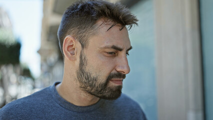 Obraz premium Cool and handsome young hispanic man, with a relaxed lifestyle, photographed outdoors with a serious expression, looking to the side on a sunny urban street.