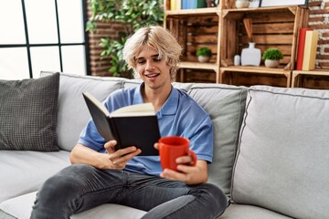 Obraz premium Young blond man reading book and drinking coffee at home