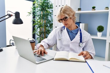 Young blond man doctor using laptop reading book at clinic