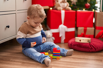 Adorable toddler playing with construction blocks sitting on floor by christmas gifts at home