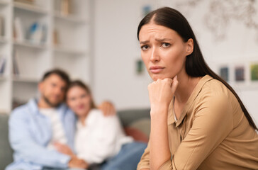 woman suffering from jealousy while man hugging another lady indoor