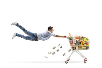 Full length shot of a casual young man flying with a shopping cart and money falling from the cart