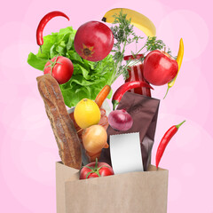 Different food products falling into paper bag on pink background