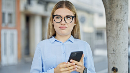 Young blonde woman business worker using smartphone with serious expression at street