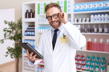 Middle age man pharmacist using touchpad working at pharmacy